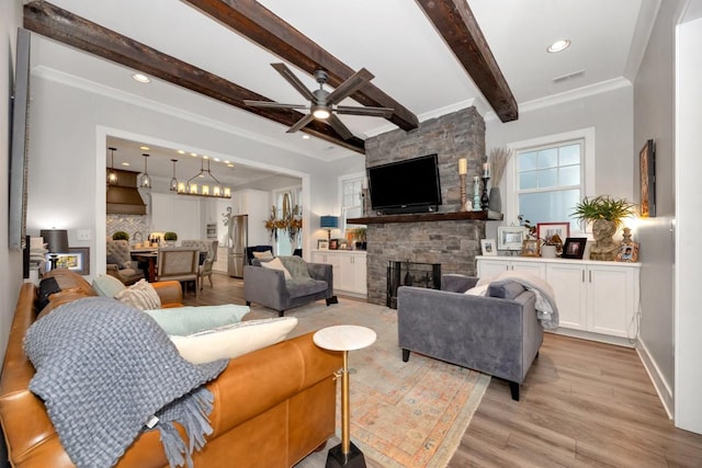 living room with light wood-type flooring, a fireplace, ceiling fan, crown molding, and beamed ceiling