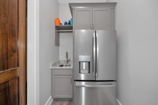 kitchen featuring light stone counters, gray cabinetry, sink, light hardwood / wood-style flooring, and stainless steel fridge with ice dispenser