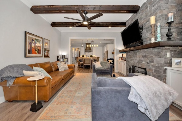 living room featuring a stone fireplace, light hardwood / wood-style flooring, ceiling fan, ornamental molding, and beamed ceiling