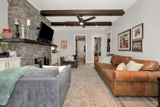 living room with beamed ceiling, ceiling fan, a stone fireplace, and light wood-type flooring