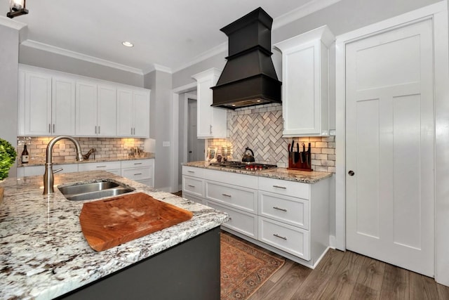 kitchen featuring dark hardwood / wood-style flooring, custom range hood, stainless steel gas cooktop, sink, and white cabinetry