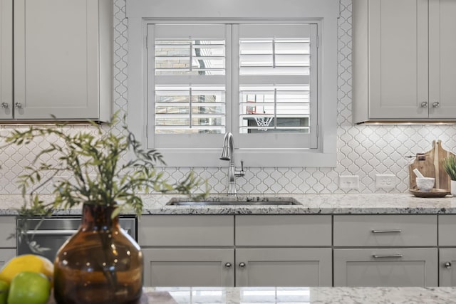 kitchen featuring decorative backsplash, light stone counters, and sink