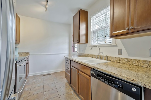 kitchen featuring light stone countertops, appliances with stainless steel finishes, light tile patterned floors, and sink