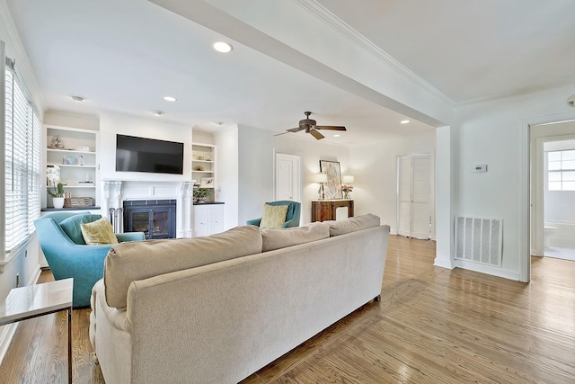 living room with built in shelves, hardwood / wood-style flooring, ceiling fan, and ornamental molding