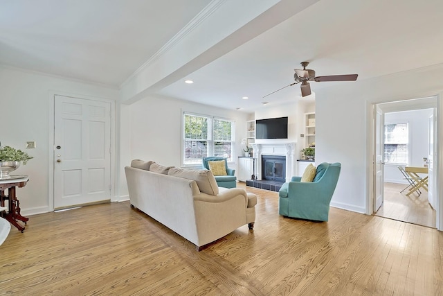 living room featuring ceiling fan, light wood-type flooring, ornamental molding, and built in shelves