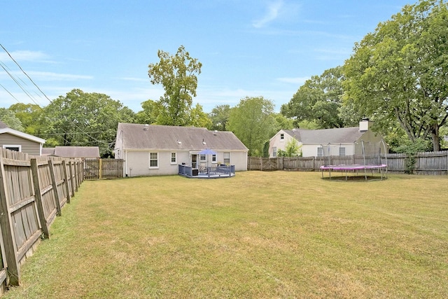 rear view of house with a lawn, a deck, and a trampoline