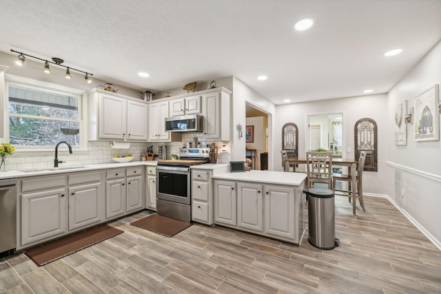 kitchen with kitchen peninsula, appliances with stainless steel finishes, backsplash, sink, and light hardwood / wood-style floors