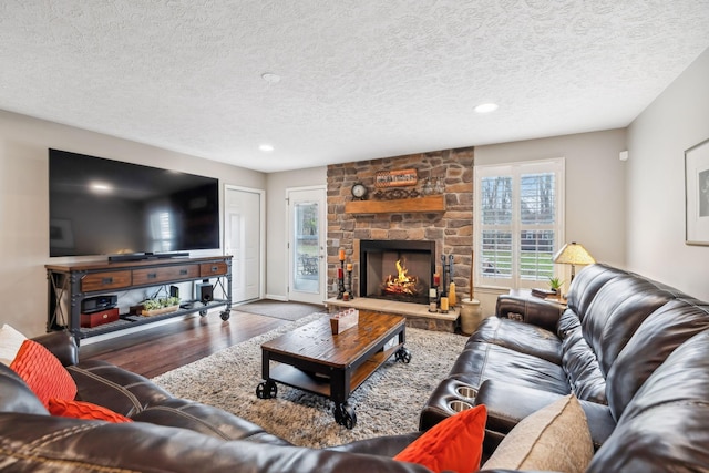 living room featuring a stone fireplace, wood-type flooring, and a textured ceiling