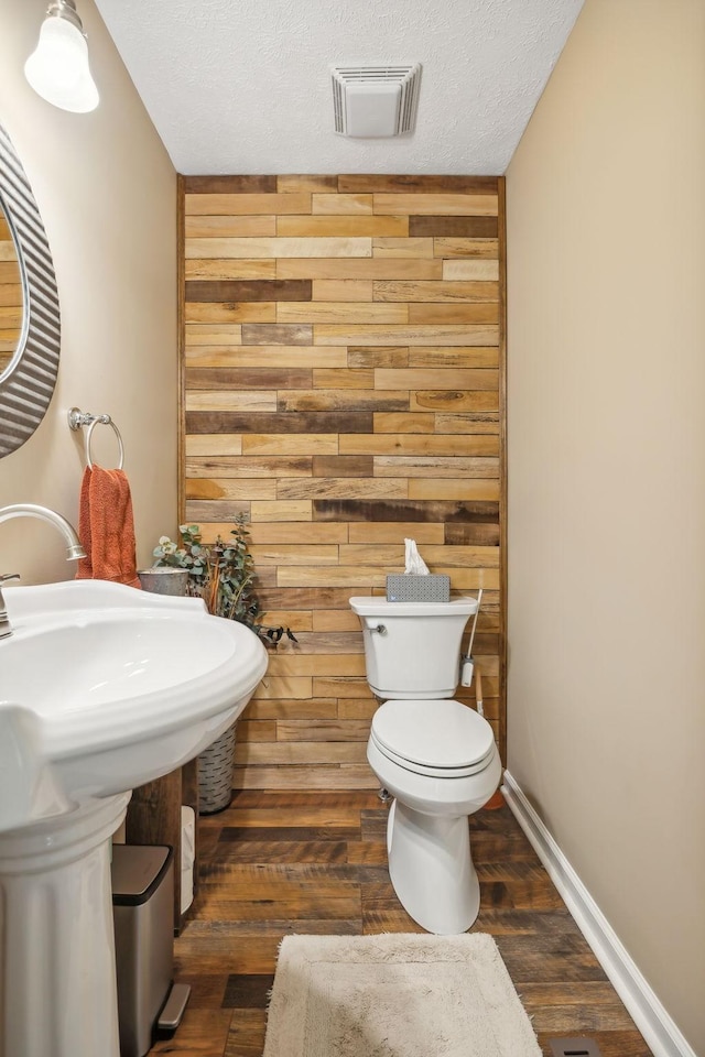 bathroom with a textured ceiling, hardwood / wood-style flooring, toilet, and wood walls