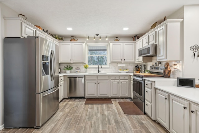 kitchen with sink, light hardwood / wood-style floors, a textured ceiling, white cabinets, and appliances with stainless steel finishes