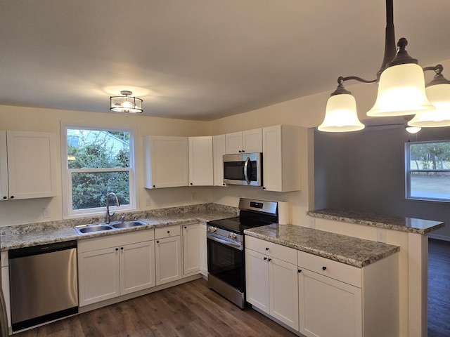 kitchen featuring white cabinetry, sink, dark wood-type flooring, hanging light fixtures, and stainless steel appliances