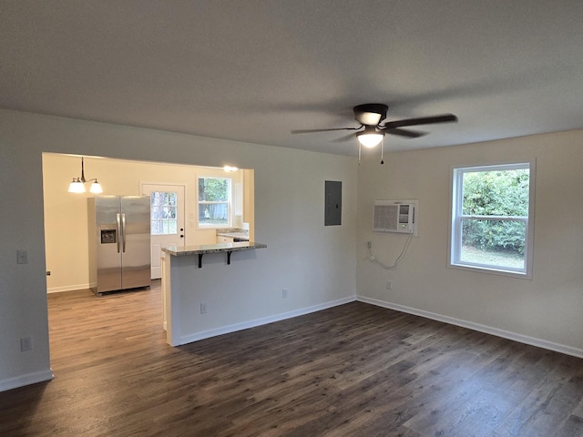 unfurnished living room featuring electric panel, a wealth of natural light, dark hardwood / wood-style flooring, and a wall mounted air conditioner