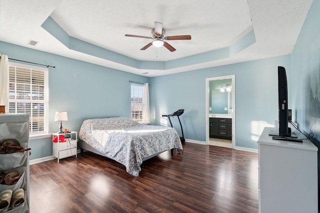 bedroom featuring ensuite bath, a textured ceiling, a tray ceiling, ceiling fan, and dark wood-type flooring