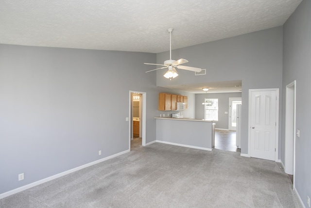 unfurnished living room with light carpet, a textured ceiling, a towering ceiling, and ceiling fan