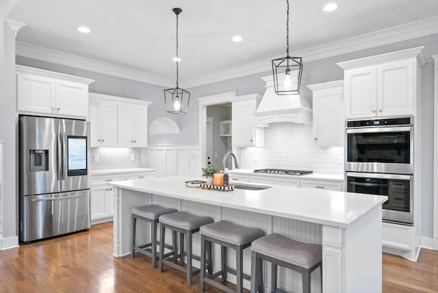 kitchen featuring white cabinetry, sink, stainless steel appliances, wood-type flooring, and a center island with sink