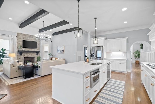 kitchen featuring white cabinetry, sink, a kitchen island with sink, a fireplace, and appliances with stainless steel finishes