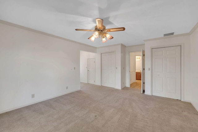 unfurnished bedroom with light carpet, multiple closets, ceiling fan, and ornamental molding