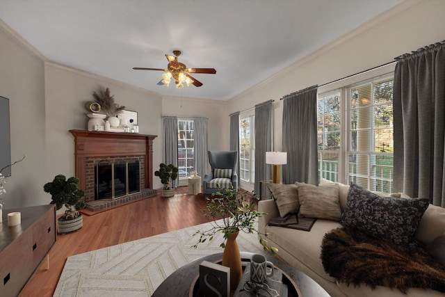 living room with hardwood / wood-style flooring, ceiling fan, ornamental molding, and a brick fireplace