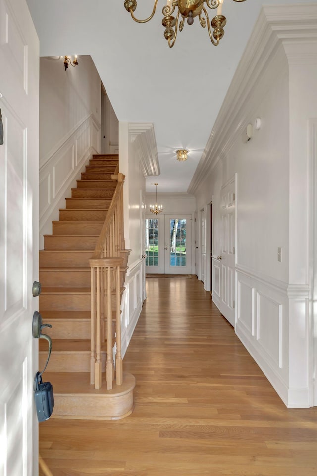 entryway featuring a notable chandelier, french doors, ornamental molding, and light hardwood / wood-style flooring