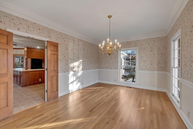 unfurnished dining area with a notable chandelier, light wood-type flooring, and crown molding