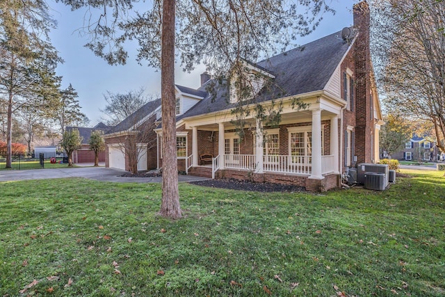 view of front facade featuring central AC unit, a garage, covered porch, and a front yard