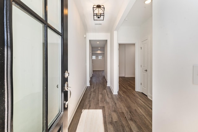 hall featuring dark wood-type flooring and an inviting chandelier