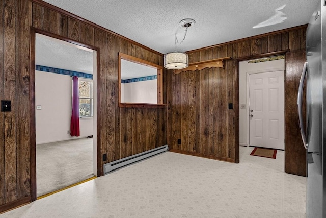 carpeted empty room featuring a textured ceiling, baseboard heating, crown molding, and wood walls