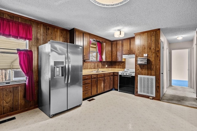 kitchen featuring stainless steel refrigerator with ice dispenser, white range, plenty of natural light, and wooden walls