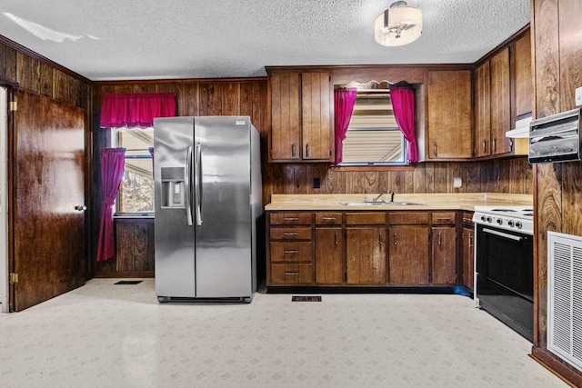 kitchen featuring stainless steel fridge with ice dispenser, stove, wooden walls, and sink