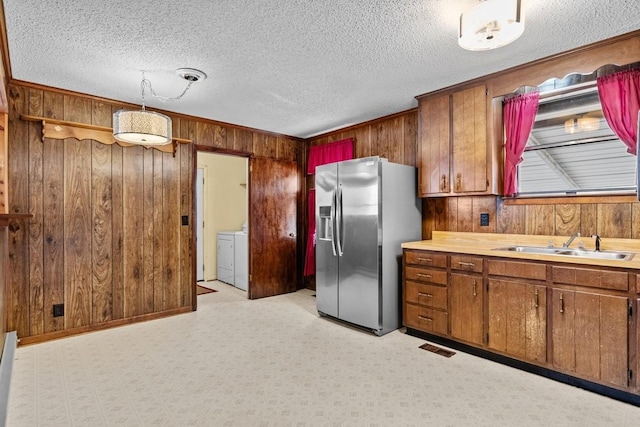 kitchen with wood walls, sink, stainless steel fridge, decorative light fixtures, and light colored carpet