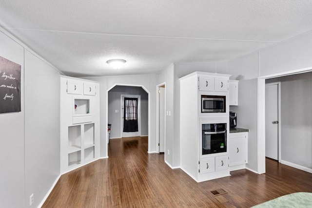 kitchen featuring a textured ceiling, white cabinetry, dark hardwood / wood-style floors, black oven, and stainless steel microwave