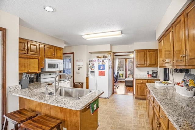 kitchen with a textured ceiling, a breakfast bar, white appliances, and sink