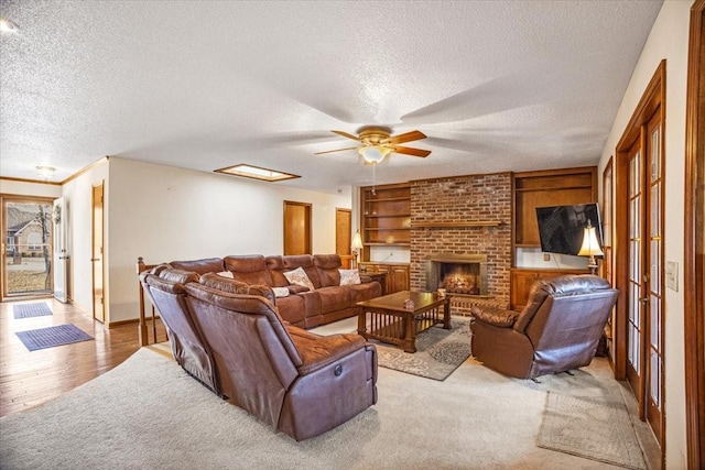 living room with ceiling fan, light hardwood / wood-style floors, a textured ceiling, and a brick fireplace