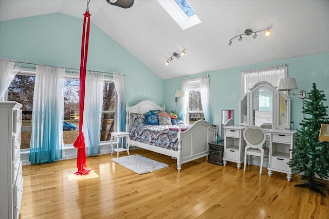 bedroom featuring rail lighting, light hardwood / wood-style flooring, and lofted ceiling with skylight