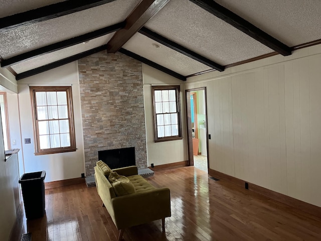 living room featuring beam ceiling, a stone fireplace, plenty of natural light, and dark hardwood / wood-style floors