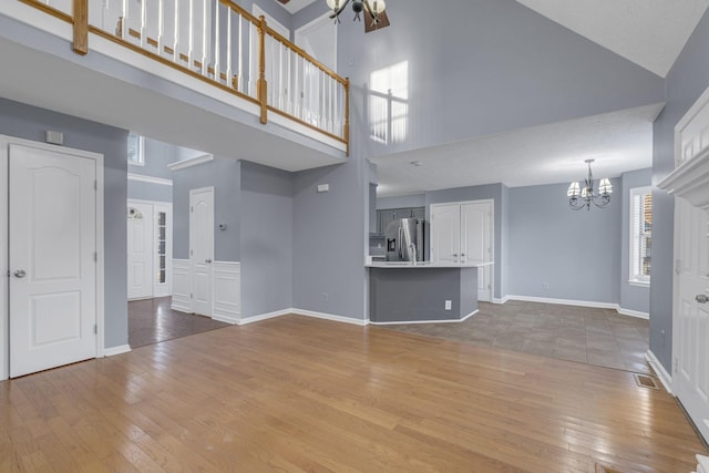 unfurnished living room featuring hardwood / wood-style flooring, high vaulted ceiling, and an inviting chandelier