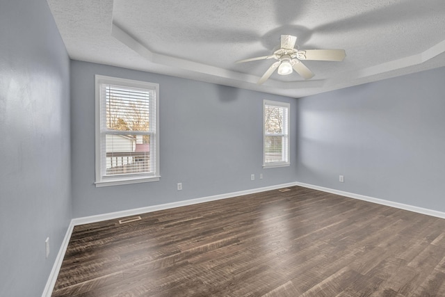 spare room with a textured ceiling, dark hardwood / wood-style floors, ceiling fan, and a tray ceiling