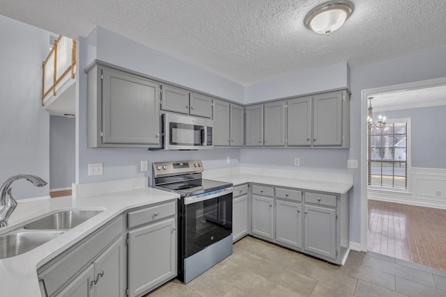 kitchen featuring appliances with stainless steel finishes, light wood-type flooring, a textured ceiling, sink, and a notable chandelier