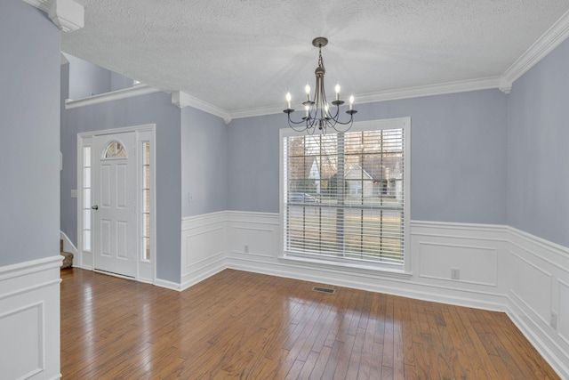 unfurnished dining area with crown molding, hardwood / wood-style floors, a chandelier, and a textured ceiling