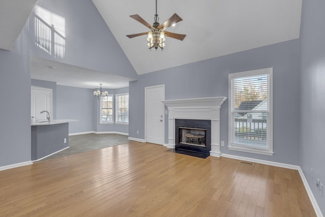 unfurnished living room with sink, high vaulted ceiling, light hardwood / wood-style floors, and ceiling fan with notable chandelier