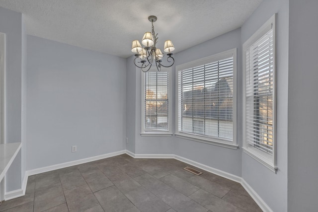 empty room featuring dark tile patterned flooring, a notable chandelier, and a textured ceiling