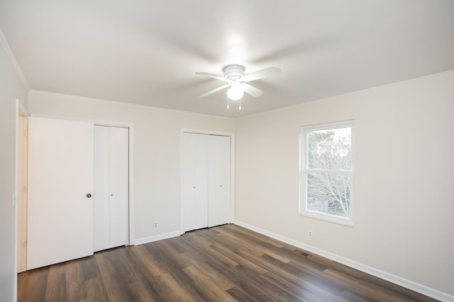 unfurnished bedroom featuring multiple closets, ceiling fan, crown molding, and dark hardwood / wood-style floors