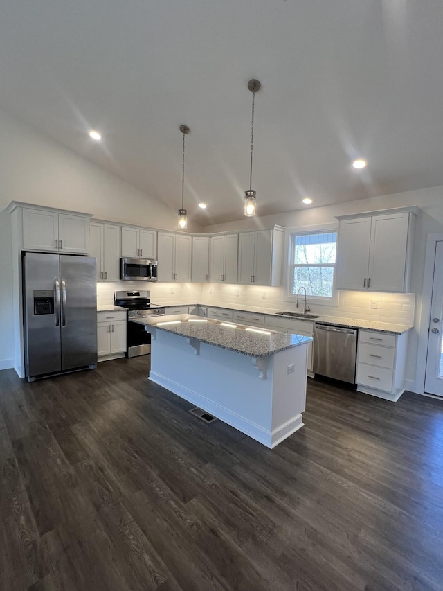 kitchen with sink, dark wood-type flooring, stainless steel appliances, a kitchen island, and decorative light fixtures