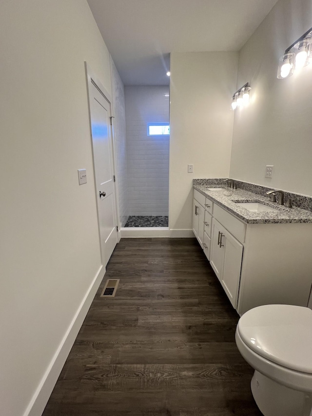 bathroom featuring hardwood / wood-style flooring, vanity, tiled shower, and toilet