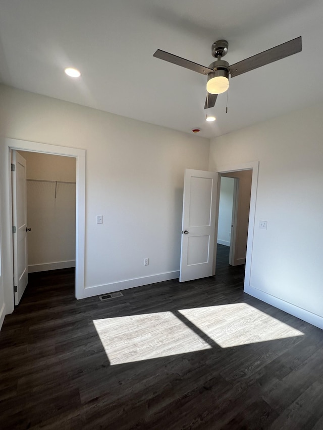 unfurnished bedroom with dark hardwood / wood-style floors, a walk in closet, a closet, and ceiling fan