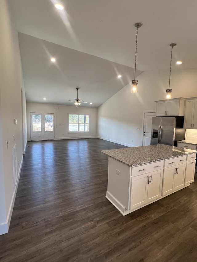 kitchen with decorative light fixtures, a center island, stainless steel fridge, light stone countertops, and white cabinets