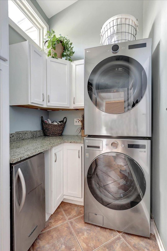 clothes washing area featuring cabinets, light tile patterned floors, and stacked washer / dryer