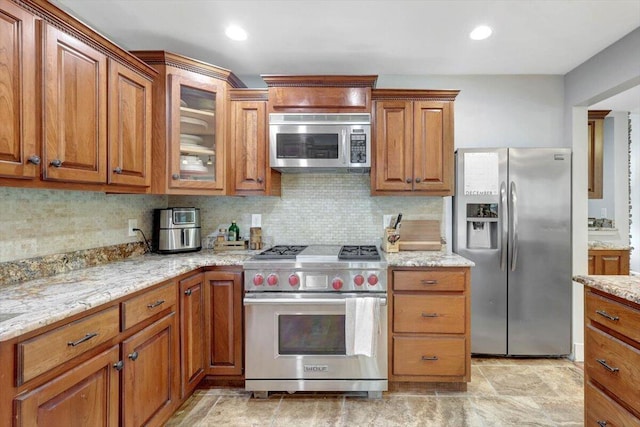 kitchen featuring decorative backsplash, appliances with stainless steel finishes, and light stone counters