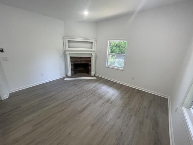 unfurnished living room with dark hardwood / wood-style flooring and a brick fireplace