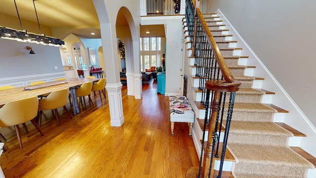 dining area featuring wood-type flooring, ornate columns, and a high ceiling